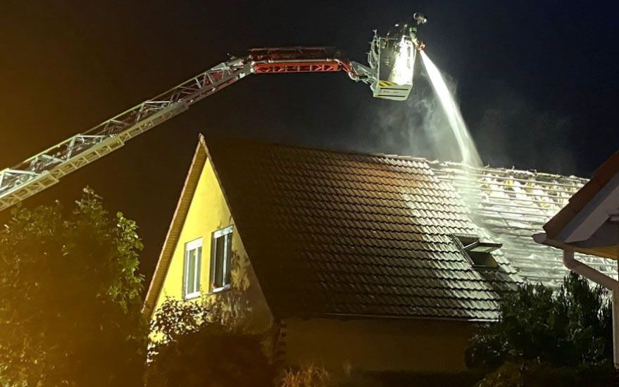 Ein Feuerwehrmann auf einem Kran versucht das Feuer über das Dach zu löschen